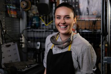 Portrait of a happy beautiful brunette female wearing working clothes and apron, standing in a workshop.